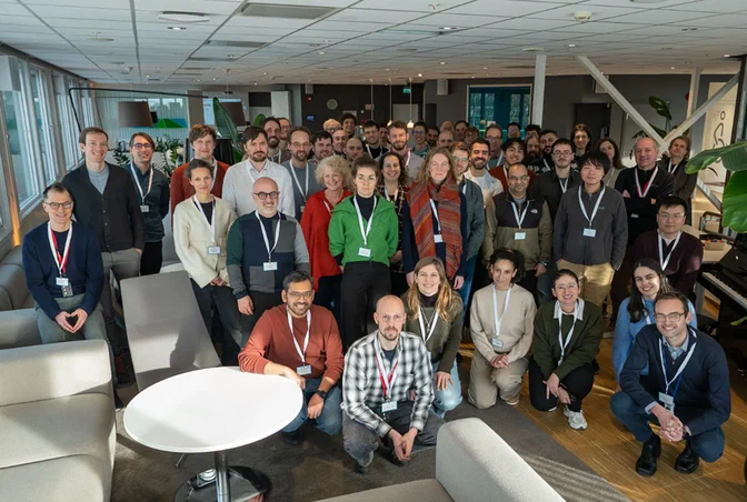 Large group of people wearing name badges gathered indoors in a modern office space, …